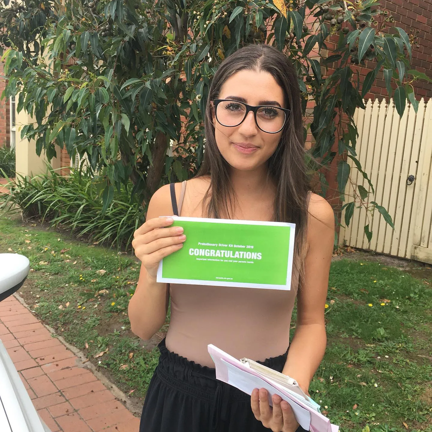 Smiling woman in glasses holding a "Probationary Driver Kit" congratulations letter.