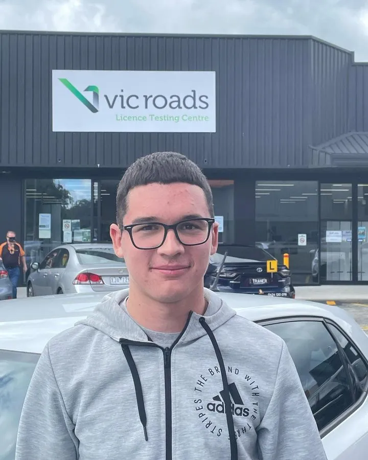 Young man with glasses standing in front of a driving license testing center.