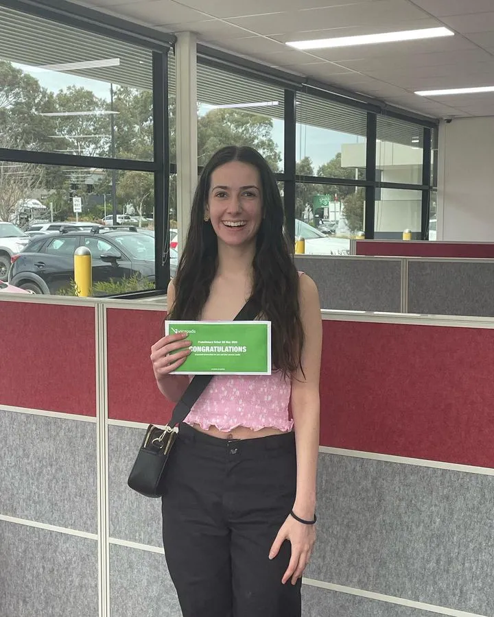 Young woman smiling, holding a "CONGRATULATIONS" certificate in an office setting
