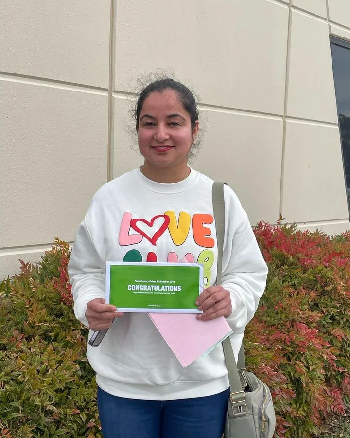 Smiling woman in a "LOVE" sweatshirt holding a green "CONGRATULATIONS" certificate