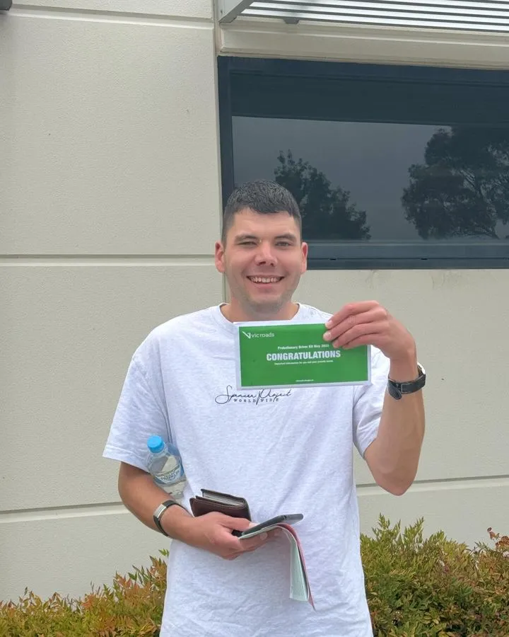 Man holding a green certificate that reads "CONGRATULATIONS" outside a building